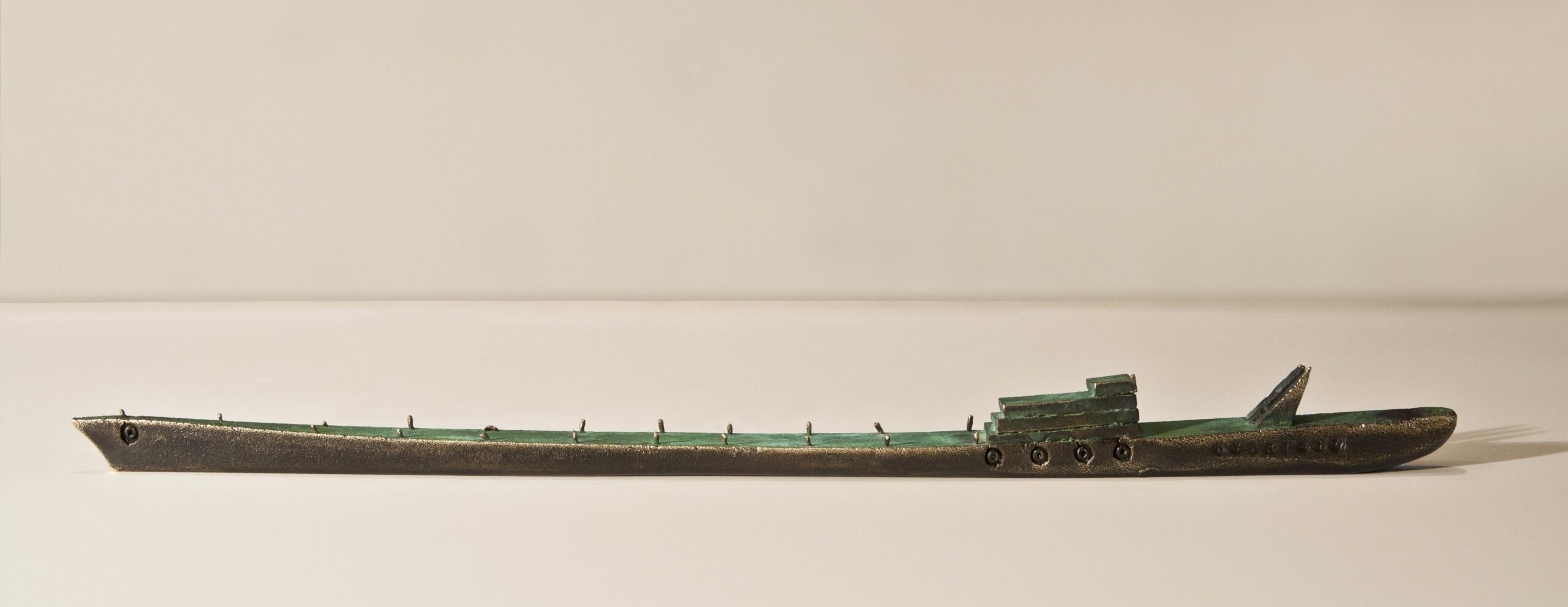 Small boat sculpture made of cast bronze with a green patina.
