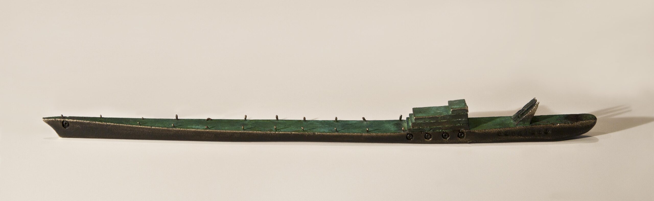 Small boat sculpture made of cast bronze with a green patina.