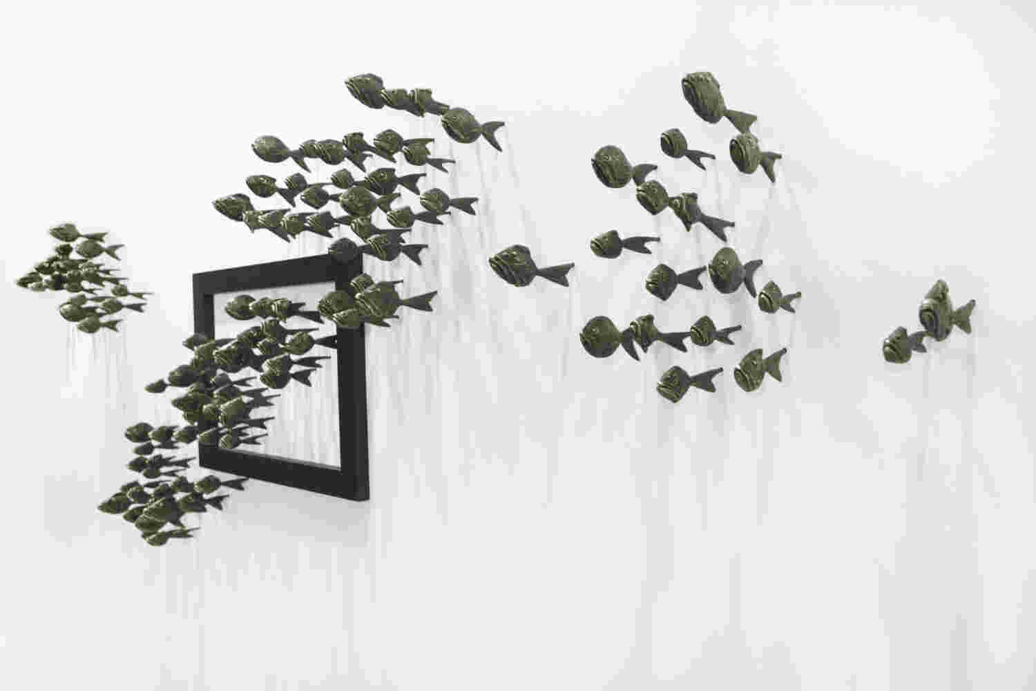 Wall installation of an explosion of fish made of cast bronze and a wooden frame.
