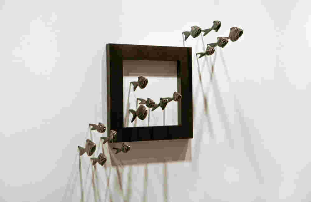 Wall installation of an explosion of fish made of cast bronze and a wooden frame.