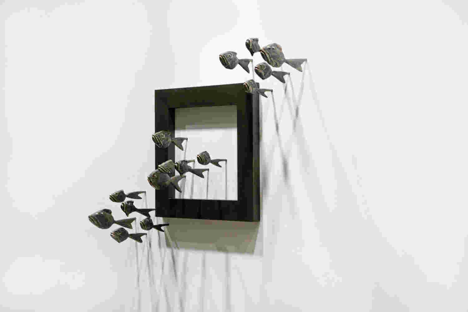 Wall installation of an explosion of fish made of cast bronze and a wooden frame.