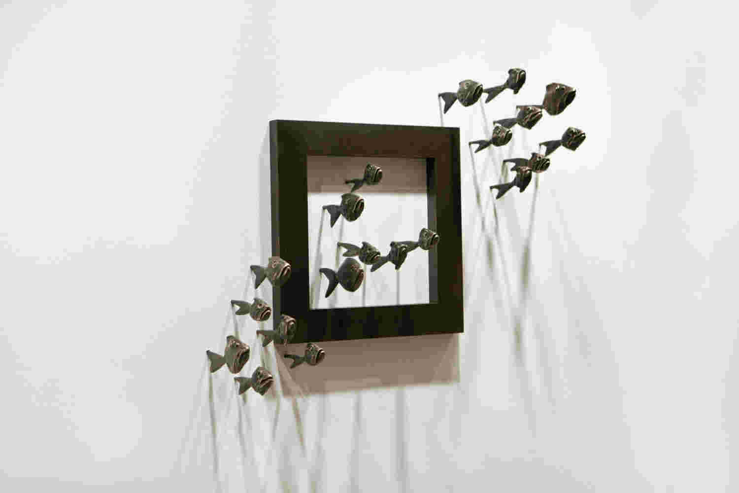 Wall installation of an explosion of fish made of cast bronze and a wooden frame.
