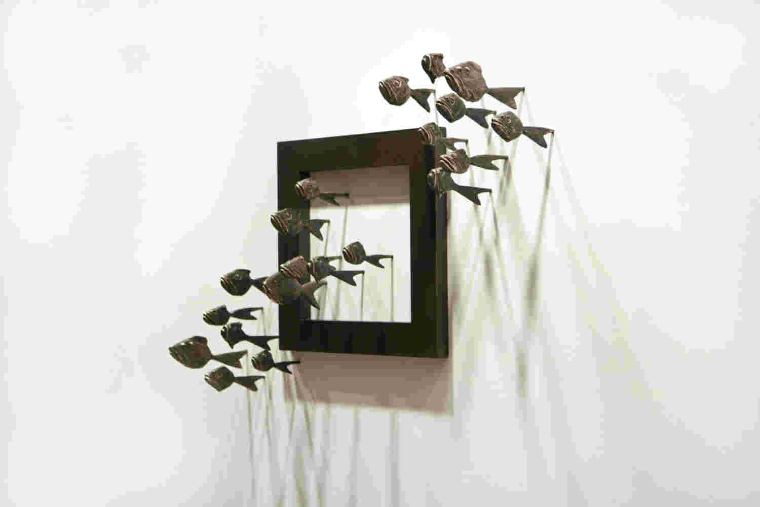 Wall installation of an explosion of fish made of cast bronze and a wooden frame.