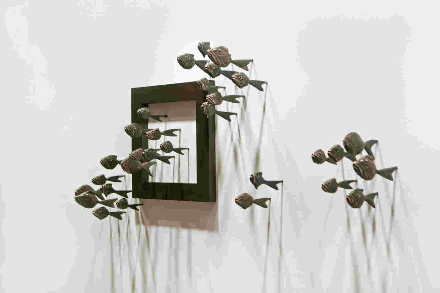 Wall installation of an explosion of fish made of cast bronze and a wooden frame.