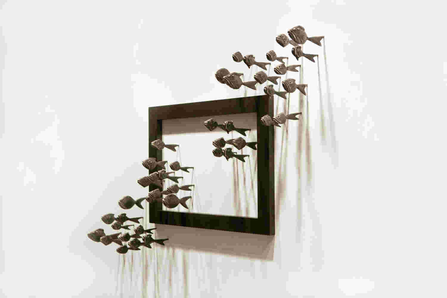Wall installation of an explosion of fish made of cast bronze and a wooden frame.