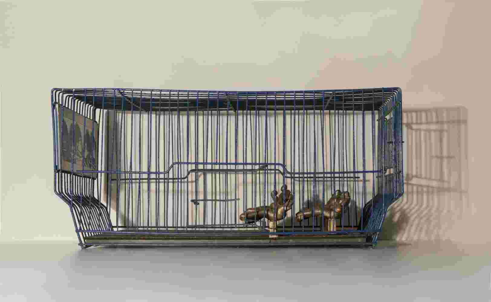 Mixed media wall sculpture of a cage and bronze people watching a projection