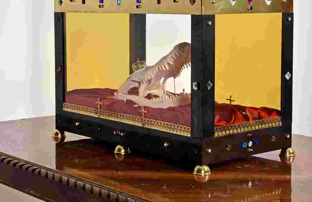 Mixed media installation of a crocodile head inside a glass casket on top of a table