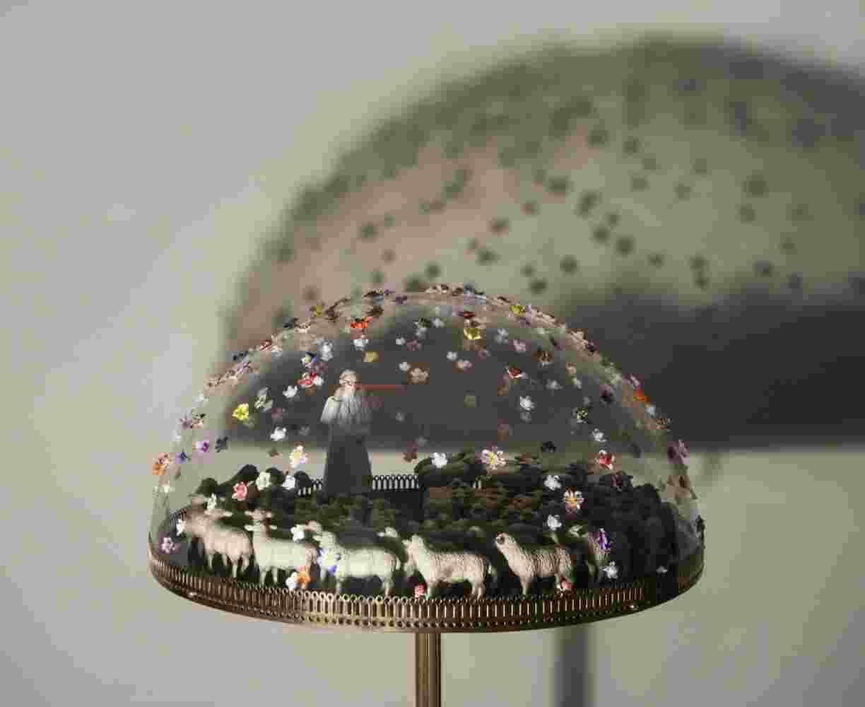 mixed media of a pope with a Pinocchio nose and sheep and colorful flowers made of plexiglass, bronze and found objects